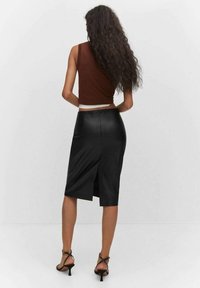 Mustat tekonahkainen hame, jossa on takalovitus, yhdistettynä ruskeaan lyhytlahkeiseen toppiin. Tekstuuri on sileä ja muotoilu istuu hyvin.