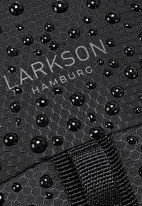 Svart texturerad tyg med vattendroppar, med präglade hexagonmönster. "LARKSON HAMBURG"-logotypen syns i vitt.