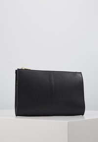 Musta nahkainen kokolaukku, jossa on teksturoitu pinta, suorakulmainen muoto ja kultainen vetoketju. Yksinkertainen ja koristelematon muotoilu.