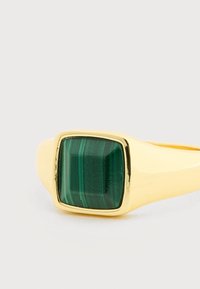 Anillo de oro con una piedra de malaquita verde de forma cuadrada que presenta estriaciones naturales, montada en una banda lisa y pulida.