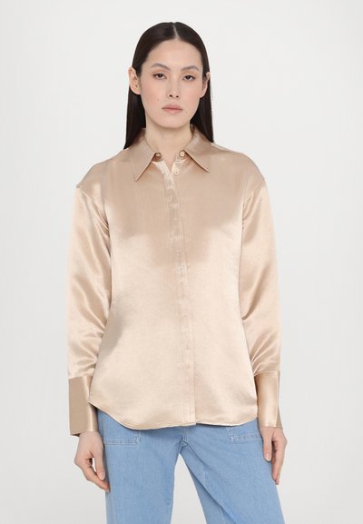 Satin long-sleeve shirt in light beige with a classic collar, button-down front, and a curved hemline, worn with blue jeans.