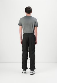 Chemise grise à manches courtes associée à un pantalon noir à taille élastique avec poches, et des baskets noir et blanc. Fond uni.