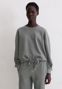 Szara bawełniana bluza z okrągłym dekoltem, luźnym krojem i wytłoczonym logo. Połączona z pasującymi szarymi dresami ze ściągaczem i bocznymi paskami.