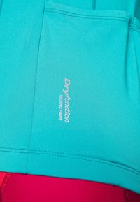 Una camiseta deportiva turquesa hecha de tela que absorbe la humedad con una textura suave, que presenta un pequeño logo blanco y costuras cosidas.