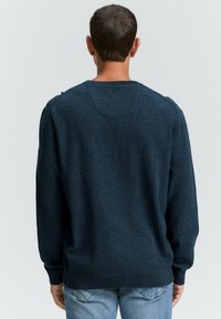 Dunkelblauer Strickpullover mit strukturiertem Finish, Rundhalsausschnitt und langen Ärmeln, kombiniert mit hellblauen Jeans. Nahtdetails an den Schultern.