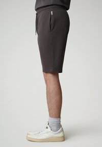 Shorts in cotone grigio misto con una vestibilità rilassata, vita elastica, cordoncino e tasche laterali, abbinati a sneakers bianche e calzini grigi.