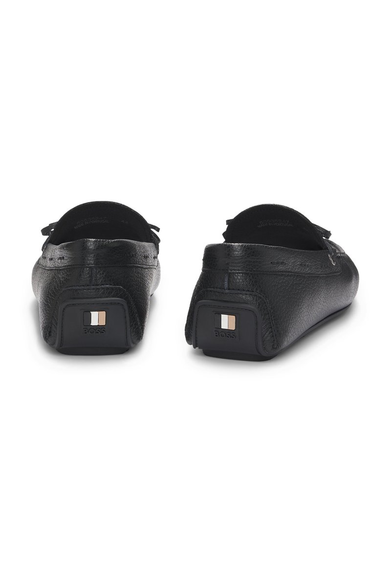 Mocassini neri in pelle con finitura testurizzata. Presentano un piccolo logo in bianco, grigio e marrone sulla parte del tallone. Suola piatta.