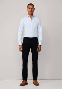 Lichtblauw overhemd met knopen, zwarte jeans en beige nette schoenen. Het overhemd heeft lange mouwen en een aansluitend model. De jeans zijn recht gesneden.