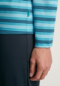 Gestreepte lang van mouw shirt in lichtblauw met marineblauwe, witte en donkerblauwe strepen, gecombineerd met een donkergroene onderkant; katoen materiaal.