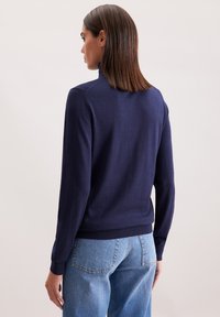 Granatowy sweter z wysokim kołnierzem, długimi rękawami i ściągaczami. Wykonany z miękkiego materiału, ma dopasowany krój i gładką fakturę.