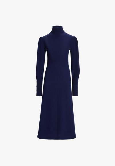 Rochie tricotată de culoare bleu marin, cu un guler înalt, mâneci lungi tip puff și accente cu nasturi pe manșete. Formă în A cu o textură netedă.