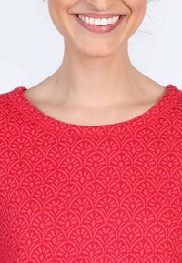 Rotes Oberteil mit einem strukturierten Muster, das Bögen ähnelt, einem glatten Ausschnitt und sichtbaren Nähten. Der Stoff wirkt weich und dehnbar.