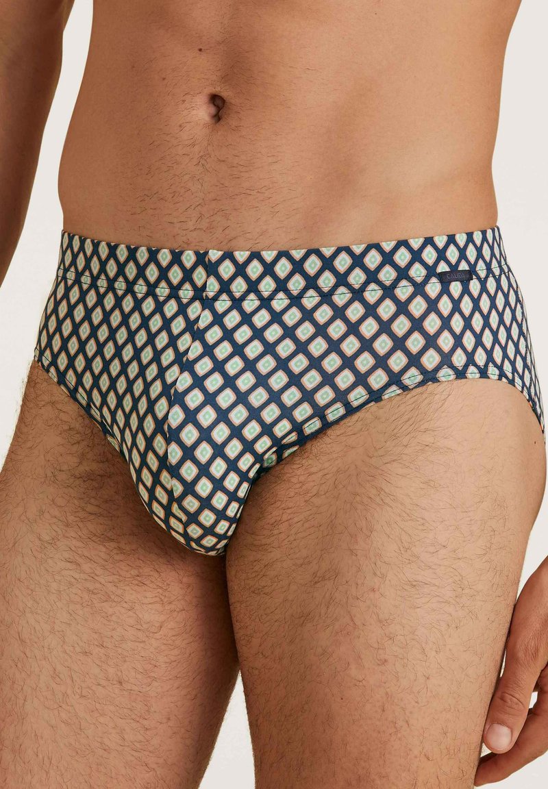 Slip da nuoto con un motivo geometrico in blu scuro, caratterizzato da diamanti blu chiaro e crema. Tessuto liscio con un design aderente.