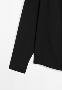 Maglietta nera a maniche lunghe con una texture liscia, caratterizzata da un polsino ripiegato e un orlo dritto. Design semplice senza ulteriori accentuazioni o motivi.
