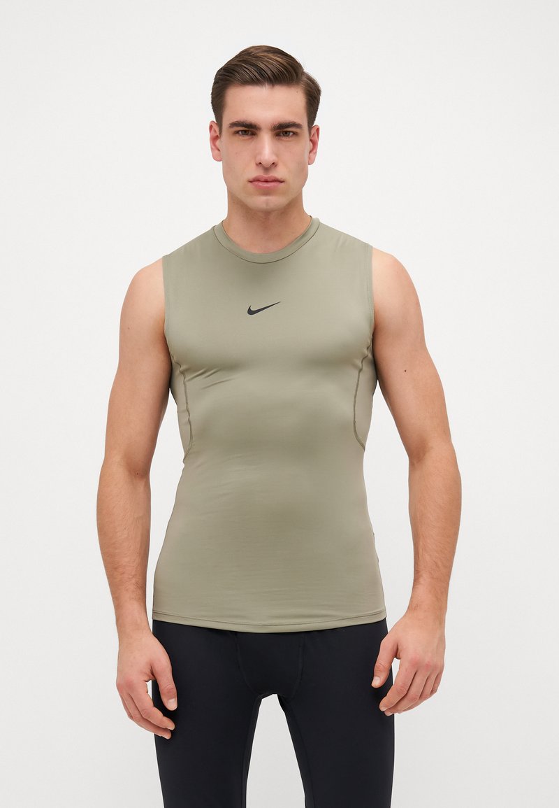 Bezrukava sportska majica u maslinasto zelenoj boji, rastezljivi materijal, prilagođeni dizajn, s crnim Nike logotipom na prsima i glatkom teksturom.