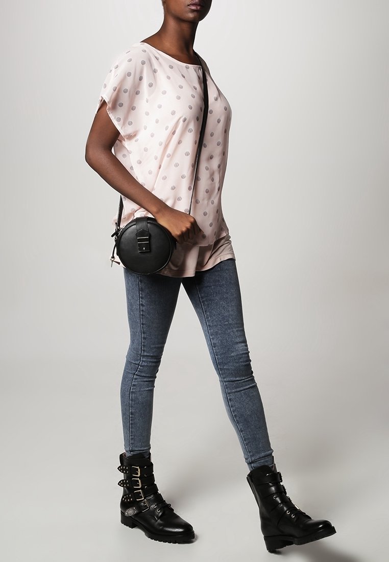 Top corto de manga corta de color rosa claro con lunares, combinado con jeans ajustados azules y botas negras hasta el tobillo con detalles de hebilla.