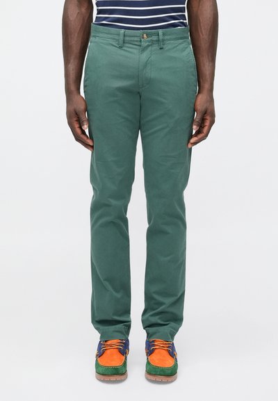 Groene chino's gemaakt van katoen, met een rechte pijp en een knoop aan de voorkant van de tailleband. Gecombineerd met kleurrijke schoenen.