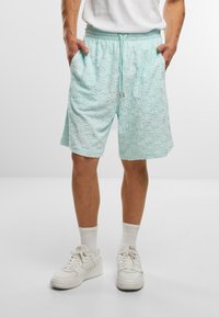 Lysblå teksturerede shorts med en snoretræk i taljen, sidelommer og et mønstret stof. Båret med hvide sneakers og hvide sokker.