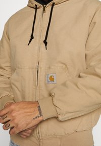 Beżowa bluza z kapturem na zamek, wykonana z bawełny, z kapturem na sznurek, prążkowanymi mankietami i łatą z logo na lewej kieszeni. Strukturalny materiał.