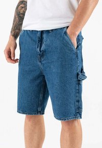 Pantalones cortos de carga de denim azul con un corte relajado, que cuentan con bolsillos laterales, un cierre de botón y dobladillos deshilachados. Textura suave con un desvanecimiento mínimo.