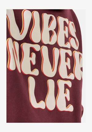 Bordeaux sweatshirt met gedurfde, golvende witte tekst met geel-oranje accenten, met de tekst "VIBES NEVER LIE". Zachte textuur, stof van gemiddelde gewicht.