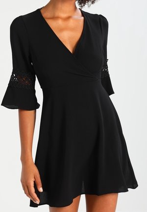 Czarna sukienka kopertowa z rozkloszowanymi rękawami ozdobionymi koronką. Miękki, lekki materiał; dekolt w serek; rozkloszowany dół; długość przed kolano.