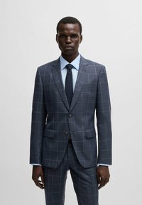 Abito a quadri blu navy con giacca a due bottoni, rever a punte e pantaloni coordinati. Camicia da uomo azzurra chiara e cravatta scura completano il look.