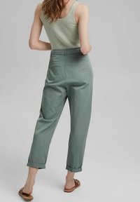 Light green ribbed tank top paired with relaxed fit slate green trousers. Trousers feature turned-up cuffs and back pockets. Brown sandals visible.