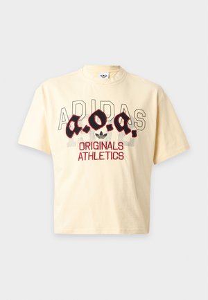 Krémsové tričko Adidas s veľkým "a.o.a." v štýlizovanej čiernej a červenej farbe, obrysovaným logom Adidas a textom "Originals Athletics" na prednej strane.