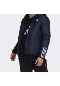 Tmavě modrá prošívaná bunda s kapucí, s bílými třemi pruhy na rukávech a logem Adidas na hrudi. Hladká textura.