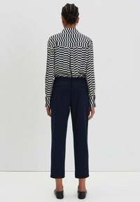 Camicia a righe bianche e nere con colletto, abbinata a pantaloni blu scuro. La camicia ha una vestibilità comoda; i pantaloni hanno una gamba dritta e una cintura.