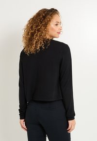 Haut noir à manches longues cropped avec un col rond. Fabriqué en tissu doux, avec une texture lisse et une coupe décontractée.
