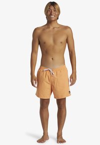 Bañador corto en naranja claro, con cintura elástica y cordón blanco, que presenta un pequeño logo negro en el lado izquierdo.