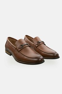 Mocasines de cuero marrón con herrajes de metal negro, suela plana y detalles de costura. Textura suave con punta redonda y diseño de fácil puesta.