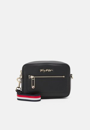 Sort rektangulær crossbody taske med forreste lynlåslomme, guldfarvet lynlås og logo, fastgjort rem i røde, hvide og marineblå striber.