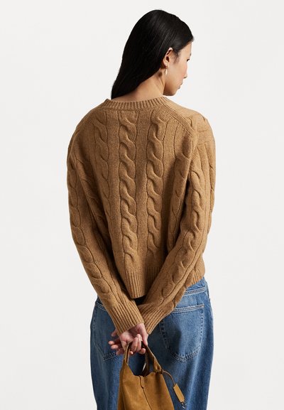 Suéter marrón de punto trenzado con un ajuste relajado, con puños y dobladillo acanalados. Combinado con unos pantalones vaqueros de cintura alta azules y un bolso en color beige.