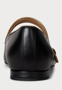 Black leather shoe with a smooth texture, featuring a gold-accented back strap and a rounded toe. Minimalist design with subtle stitching.