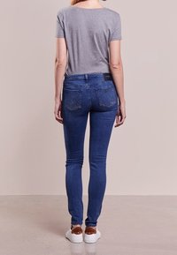 Trånga jeans i medelblå denim med bakfickor prydda med silvernitar, tillsammans med en grå t-shirt och vita sneakers.