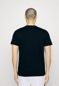 Camiseta de algodón negra con mangas cortas y escote redondo. Textura suave, sin patrones ni adornos visibles. Vista trasera mostrada.