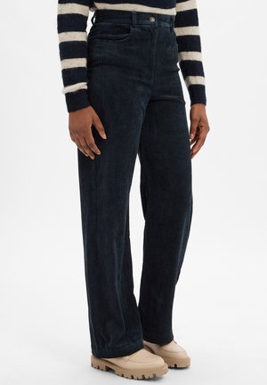 Marineblaue Cord-Hosens mit weitem Bein, gerippter Textur, hoher Taille, vorderen Taschen und einem metallenen Knopfverschluss, kombiniert mit beigen Plateauschuhen.