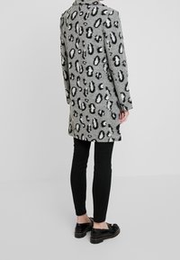 Grijze jas met zwart luipaardprint, gemaakt van zacht materiaal. Heeft lange mouwen en een rechte snit. Gekocht met zwarte leggings en schoenen.
