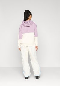 Sweatshirt com capuz em lavanda e creme, com um design em bloco. Combinado com calças largas de cor clara e calçado preto.