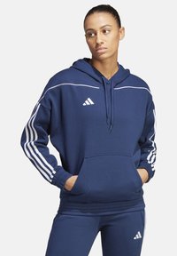 Marineblaue Kapuzenjacke mit weißen Streifen entlang der Ärmel und Schulter, Kängurutasche und Kordelzugkapuze, aus weichem Stoff.