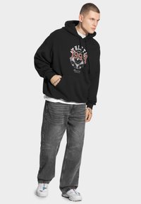 Czarna bluza z kapturem z graficznym nadrukiem, z czerwonym i białym napisem. Połączona z szarymi dżinsami i białymi trampkami.