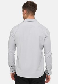 Lichtgrijze blouse met lange mouwen, een kraag, gebuttonneerde manchetten en een gladde textuur. Heeft een rechte achterkant zonder zakken of patronen.
