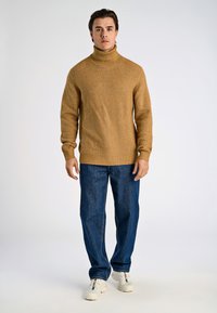 Senapsgul ribbstickad polotröja kombinerad med blå jeans och vita sneakers, med avslappnad passform och texturerat tyg.