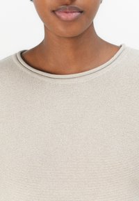 Suéter de malha bege com decote arredondado e tecido texturizado, apresentando um padrão subtil na trama. Vista aproximada da parte superior do corpo.