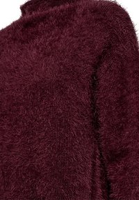 Burgundy fluffig tröja med hög hals; har en mjuk, texturerad stickning och en något oversized passform. Tyget har ett distinkt, fluffigt utseende.