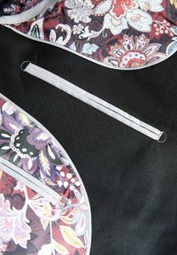 Black fabric bag with colorful floral lining, includes grey trim and a horizontal pocket. Features intricate patterns and textures.
