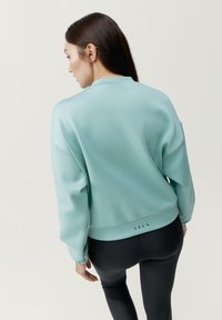 Jasnoniebieski sweatshirt o luźnym kroju, z długimi rękawami, ściągaczami oraz stylowym, skróconym hemem z trójkątnymi wycięciami z tyłu.